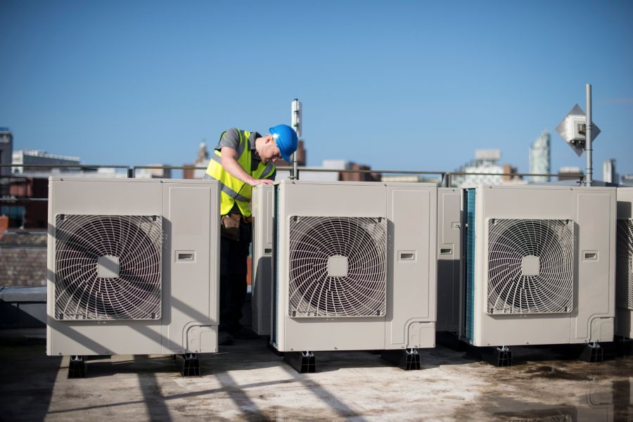 A man in yellow vest standing next to air conditioning units.