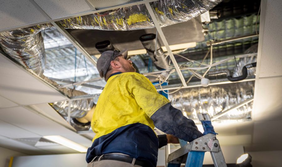 A man in yellow shirt on ladder near ceiling.