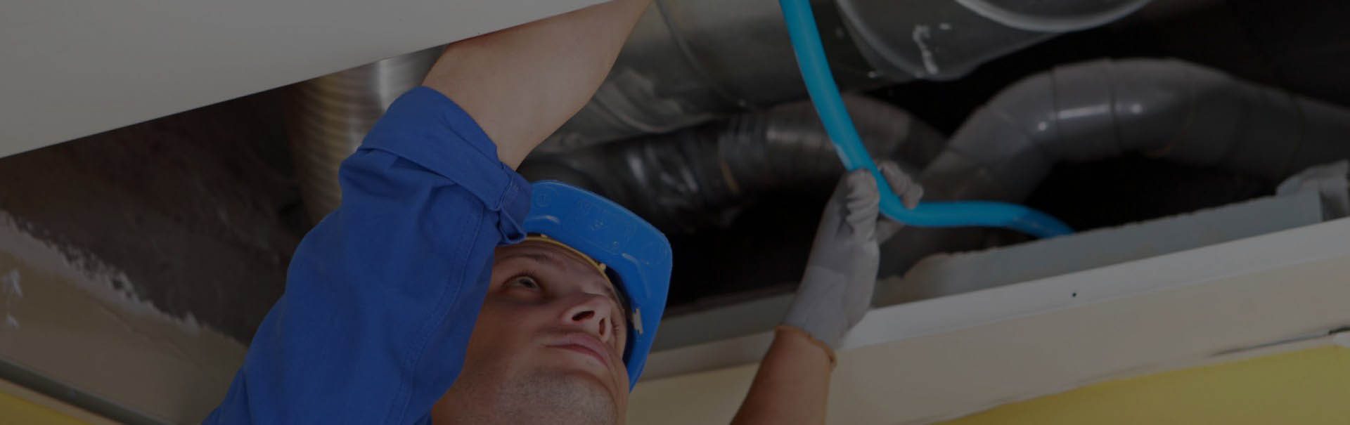 A man in blue shirt holding pipe near ceiling.