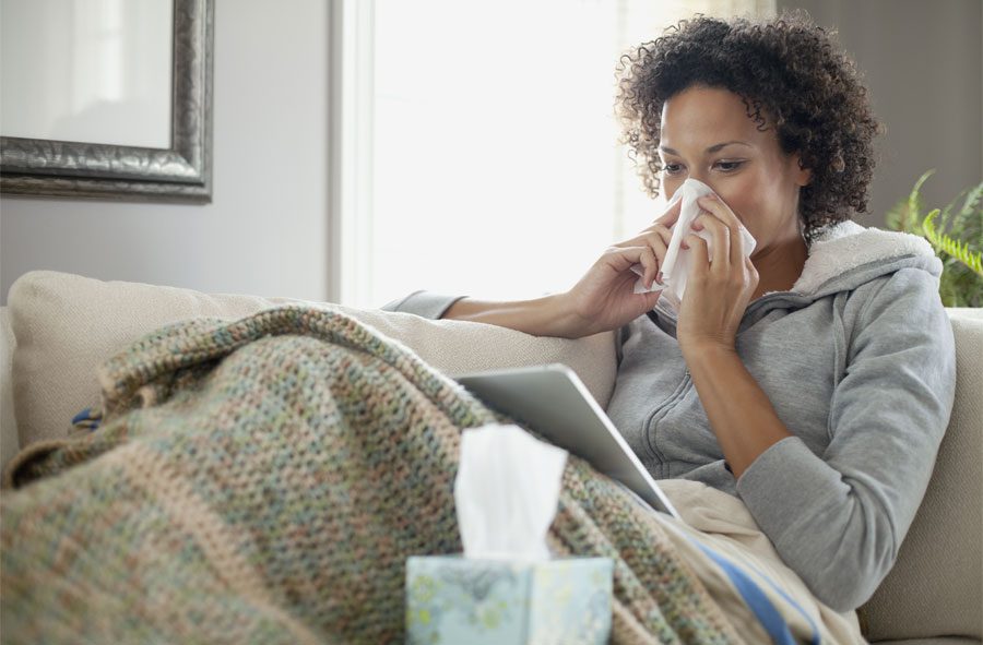 A woman sitting on the couch blowing her nose.